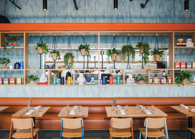 The kitchen was left partially visible in the main dining area behind a bookcase divider styled with products, accessories and greenery. Image curtesy of The Plaid Penguin