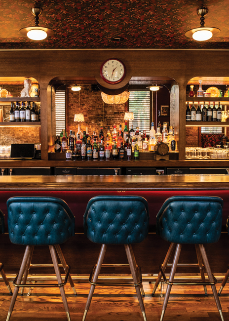 To make it a focal point, the original bar was lengthened and a high-lacquer red wall covering was added to the top half of its face, against which teal blue barstools pop.
